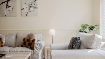 A living room with a sofa, a coffee table, and a lamp. There are two wall-mounted artworks and a potted plant.
