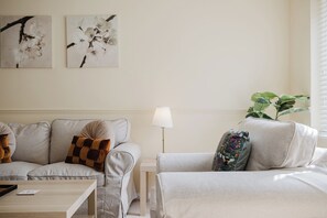 Sala de estar con sofá, una mesa de centro y una lámpara. Hay dos obras de arte colgadas en la pared y una planta en maceta.