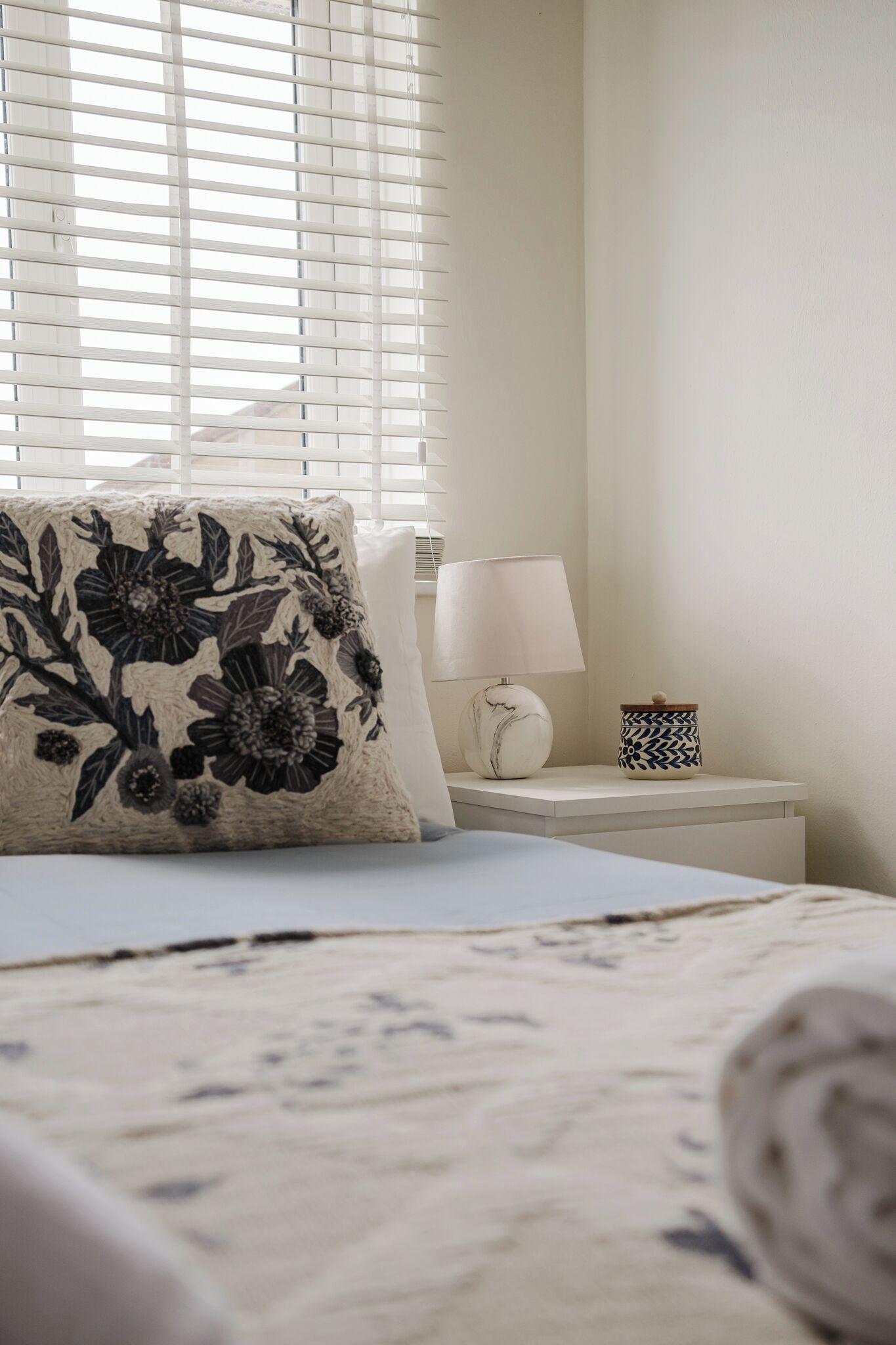 Une chambre à coucher avec un lit, une table de chevet, une lampe et une fenêtre avec des stores.
