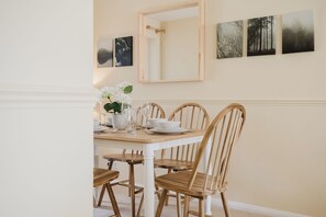 Un comedor con una mesa de madera y cuatro sillas, un florero con flores y tres cuadros en la pared.