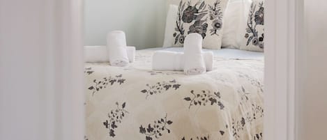 A bedroom with a bed, pillows, a bedside table, and a hanging light fixture.