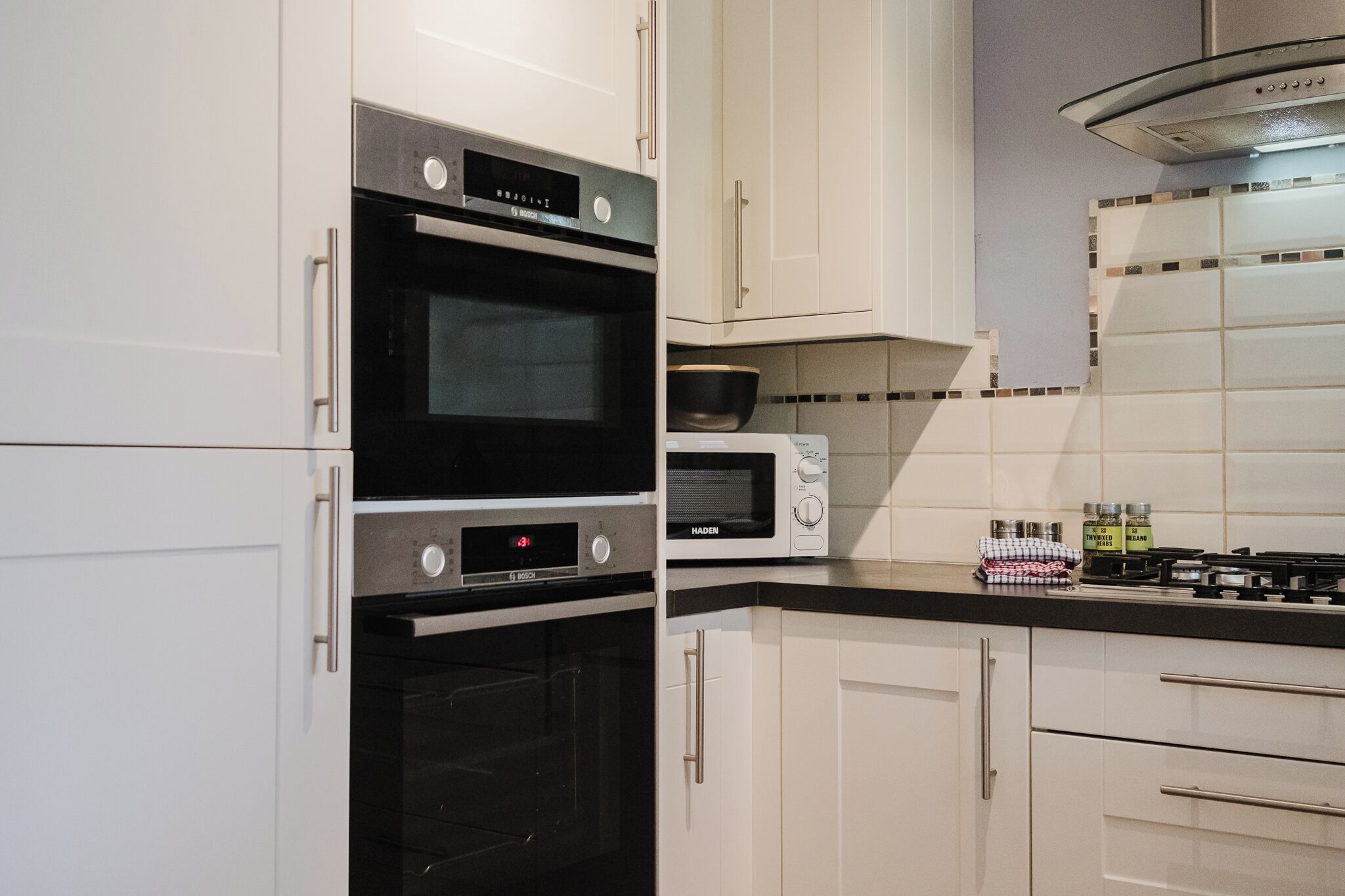 A kitchen with white cabinets, a Bosch oven, a microwave, and a stove.