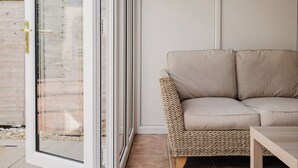 Una habitación con un sofá de mimbre, una mesa de madera y un ventanal corredero que da a un espacio exterior.