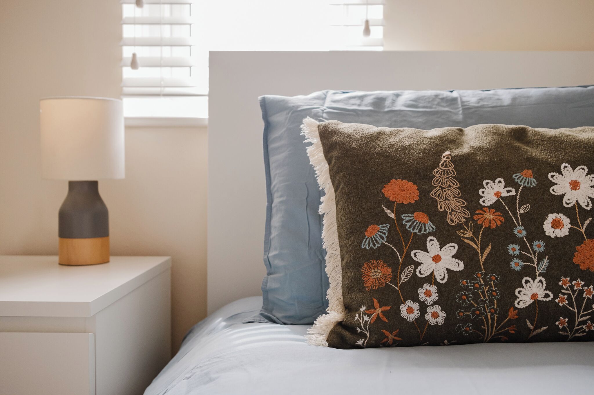 Un lit avec un oreiller bleu et un coussin décoratif orné de broderies florales.