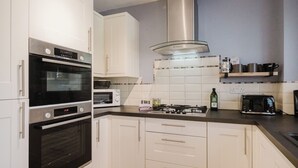 Una cocina moderna con gabinetes blancos, horno empotrado, microondas, estufa a gas y cafetera.