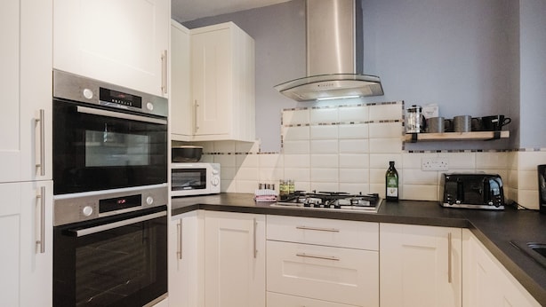 Une cuisine moderne avec des meubles blancs, un four encastré, un four à micro-ondes, une cuisinière à gaz et une machine à café.