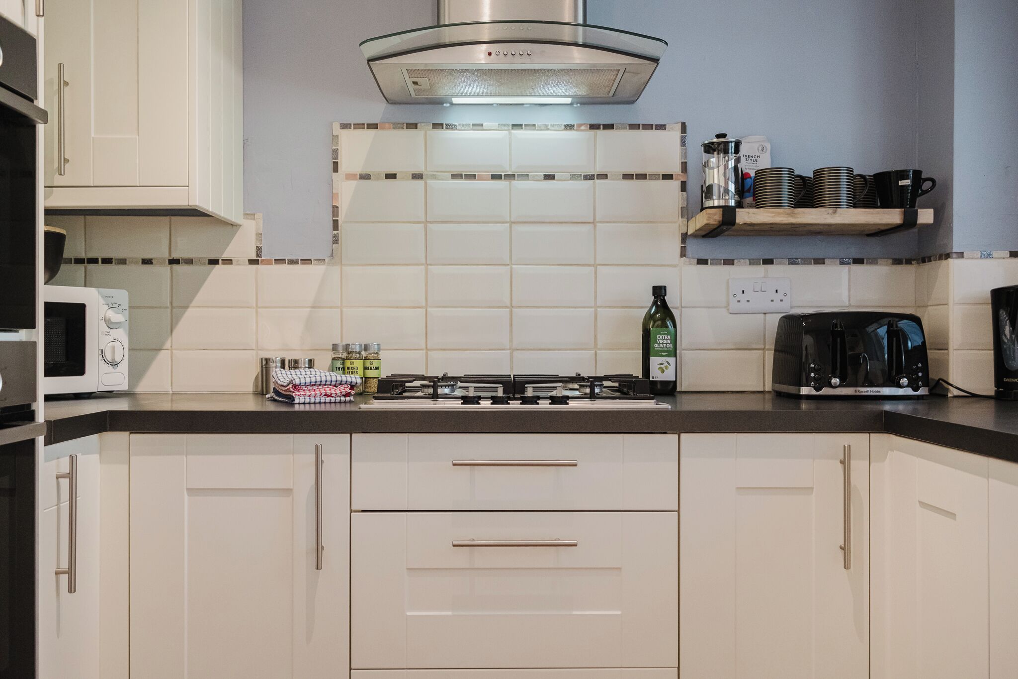 A kitchen with white cabinets, a gas stove, a microwave, and a coffee maker.