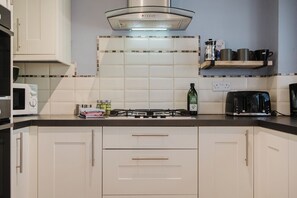 Una cocina con gabinetes blancos, estufa a gas, microondas y cafetera.