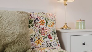 Un lit bien fait, avec une couette et des oreillers à motifs floraux, une lampe de chevet et une petite table de chevet sur laquelle se trouve un récipient vert.