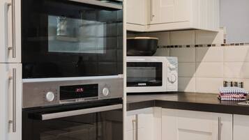 Uma cozinha com armários brancos, um forno Bosch, micro-ondas e fogão.