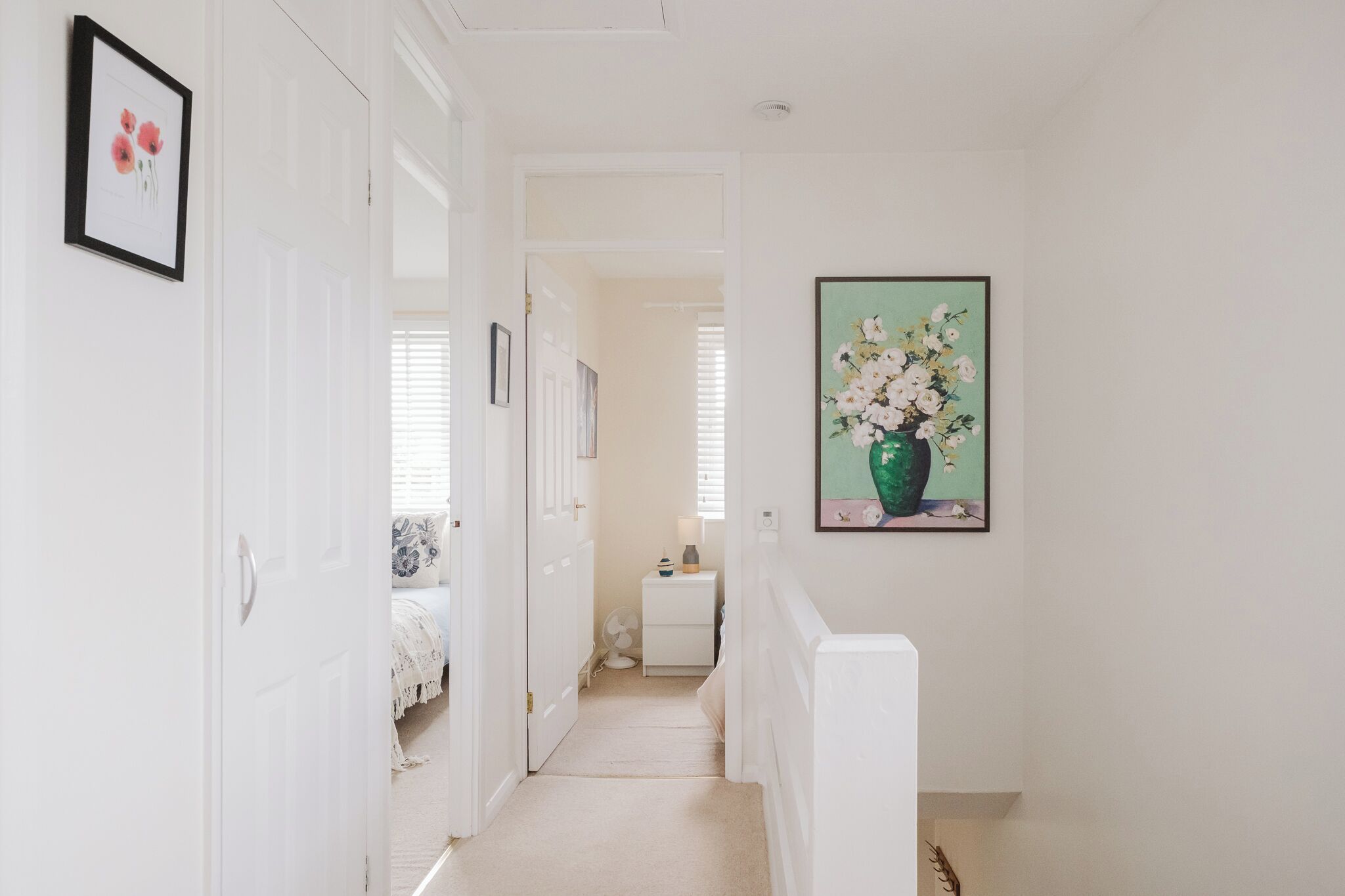 A hallway with white walls, a door on the left, and a framed painting on the right.