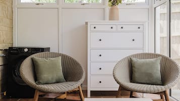 A room with two wicker chairs, a white dresser, and a washing machine.
