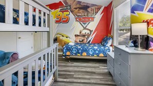 Een kinderkamer met een muurschildering van personages uit 'Cars', stapelbedden, een bureau en een raam met jaloezieën.