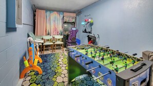 Een kamer met een tafelvoetbaltafel, een kleurrijk tapijt en een muurschildering van een stadsgezicht.