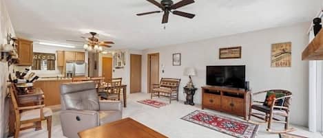 A spacious living room with a ceiling fan, a television, and a dining area with wooden furniture.