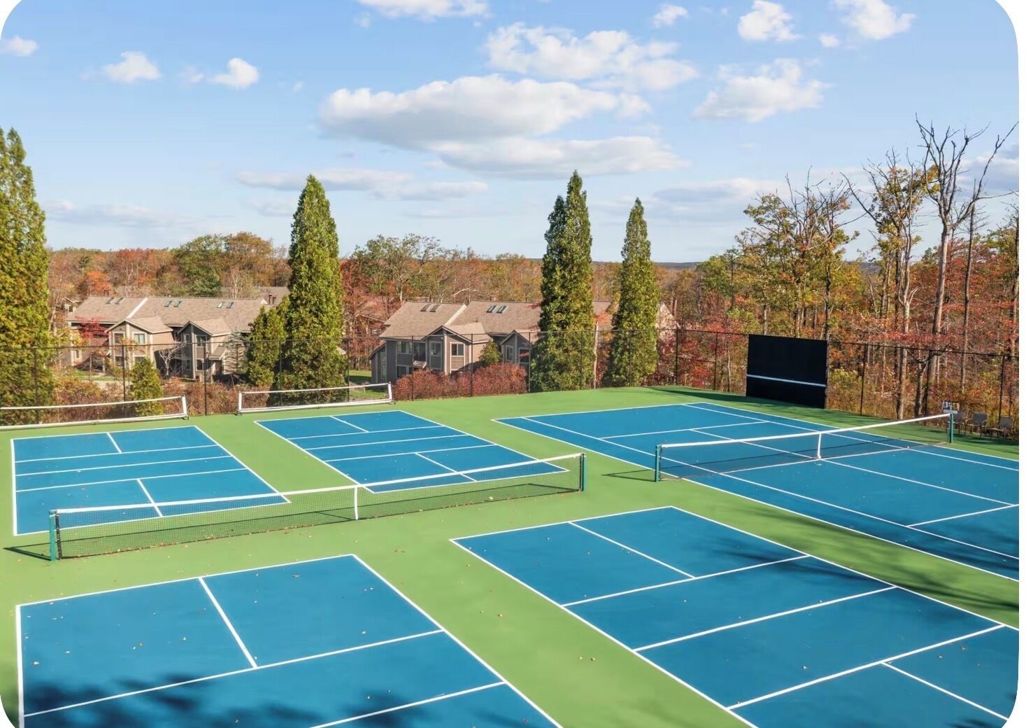 Ein Tennisplatzkomplex mit mehreren Plätzen, umgeben von Bäumen und Wohnhäusern.