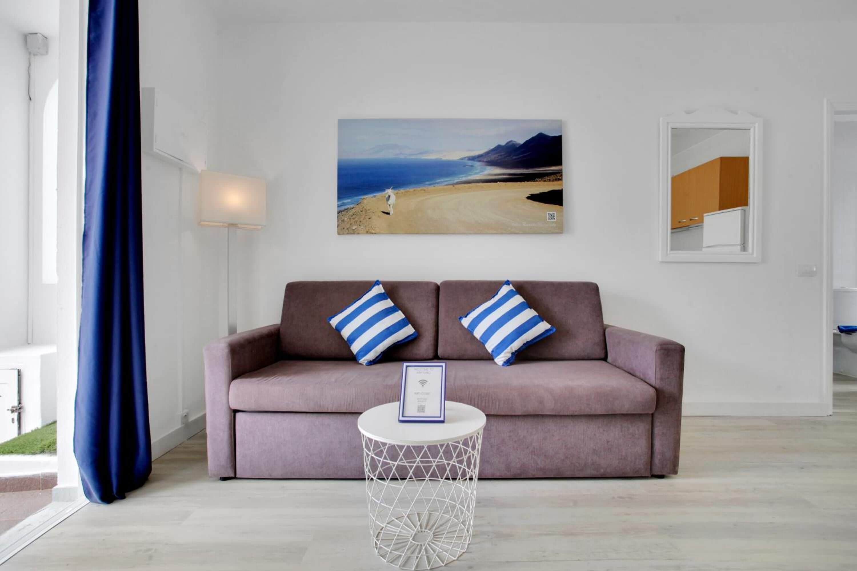 A living room with a sofa, two pillows, a round coffee table, and a painting of a beach scene.