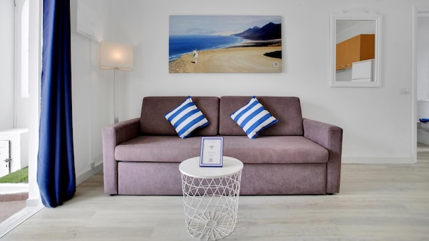 Un soggiorno con divano, due cuscini, un tavolino rotondo e un quadro raffigurante una spiaggia.