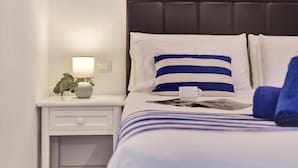 Un letto rifatto con lenzuola a righe bianche e blu, un comodino bianco con una lampada e una piccola pianta.