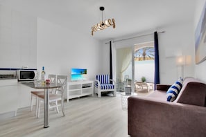 A modern living room with a flat-screen TV, a dining area with a table and chairs, a sofa, and a ceiling light fixture. - Neptuno Bungalows (La Oliva)