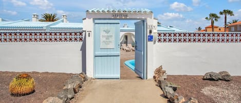 A hotel entrance with a blue door, a pool area, and a decorative fence.