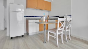 Una cucina compatta con un frigorifero bianco, mobili in legno, un piano di lavoro in granito e due sedie bianche.