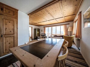 A spacious room with a large wooden table, a sofa, and a window with curtains. - Chesa Quadrellas / OG by Interhome (Samedan)