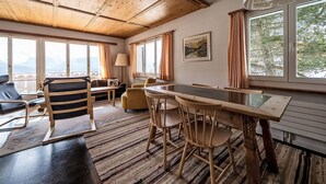 Ein Zimmer mit Holzboden, einem Esstisch mit Stühlen, einer Couch und einem Fenster mit Vorhängen.