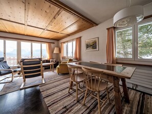 Ein Zimmer mit Holzboden, einem Esstisch mit Stühlen, einer Couch und einem Fenster mit Vorhängen.