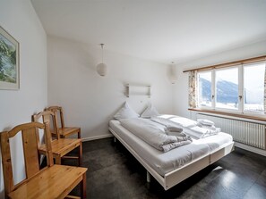 A bedroom with a bed, two chairs, a radiator, and a window with a view of mountains. - Chesa Quadrellas / OG by Interhome (Samedan)