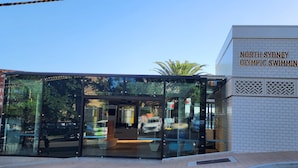 Een modern gebouw met een glazen gevel en een bord waarop 'North Sydney Olympic Swimming Pool' staat.