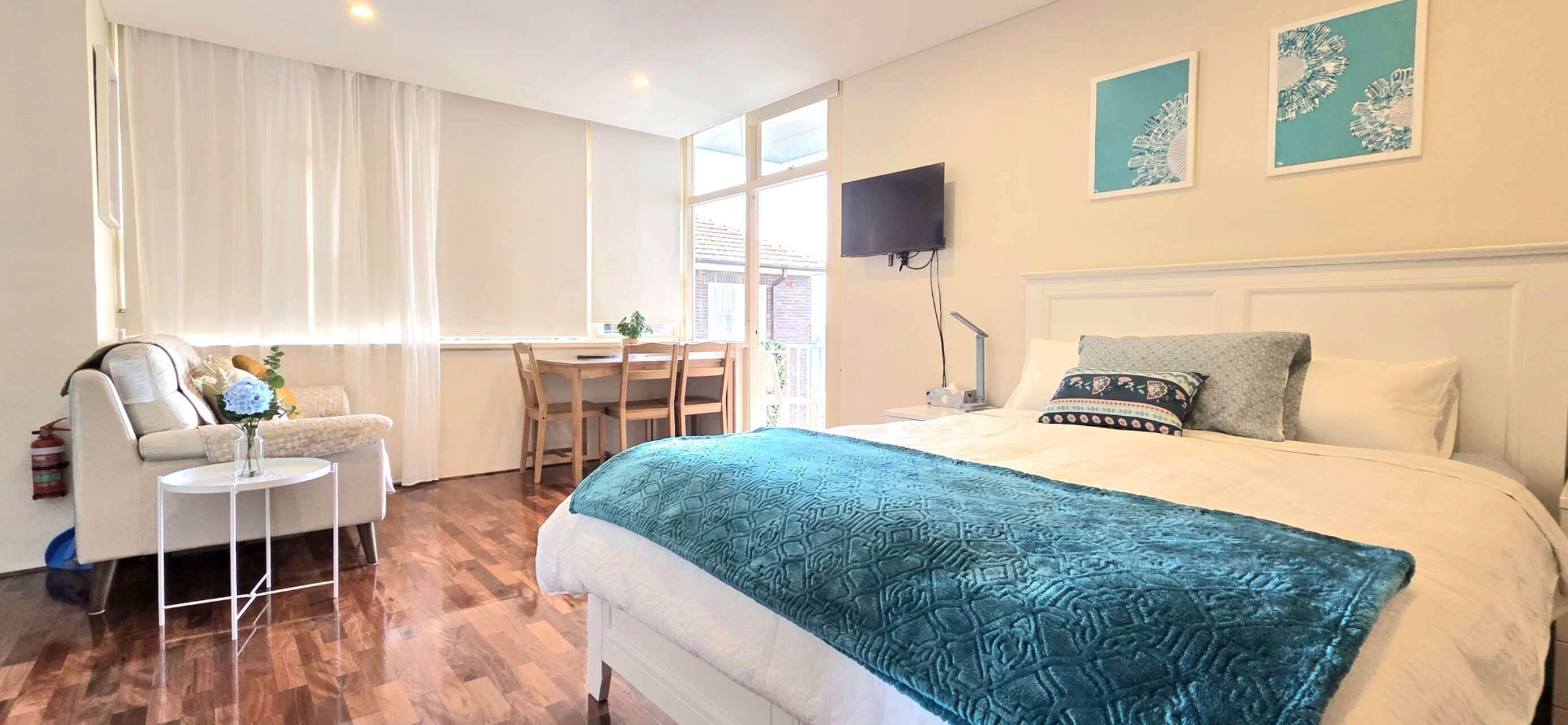 A bedroom with a bed, a desk, a chair, a TV, and artwork on the wall.