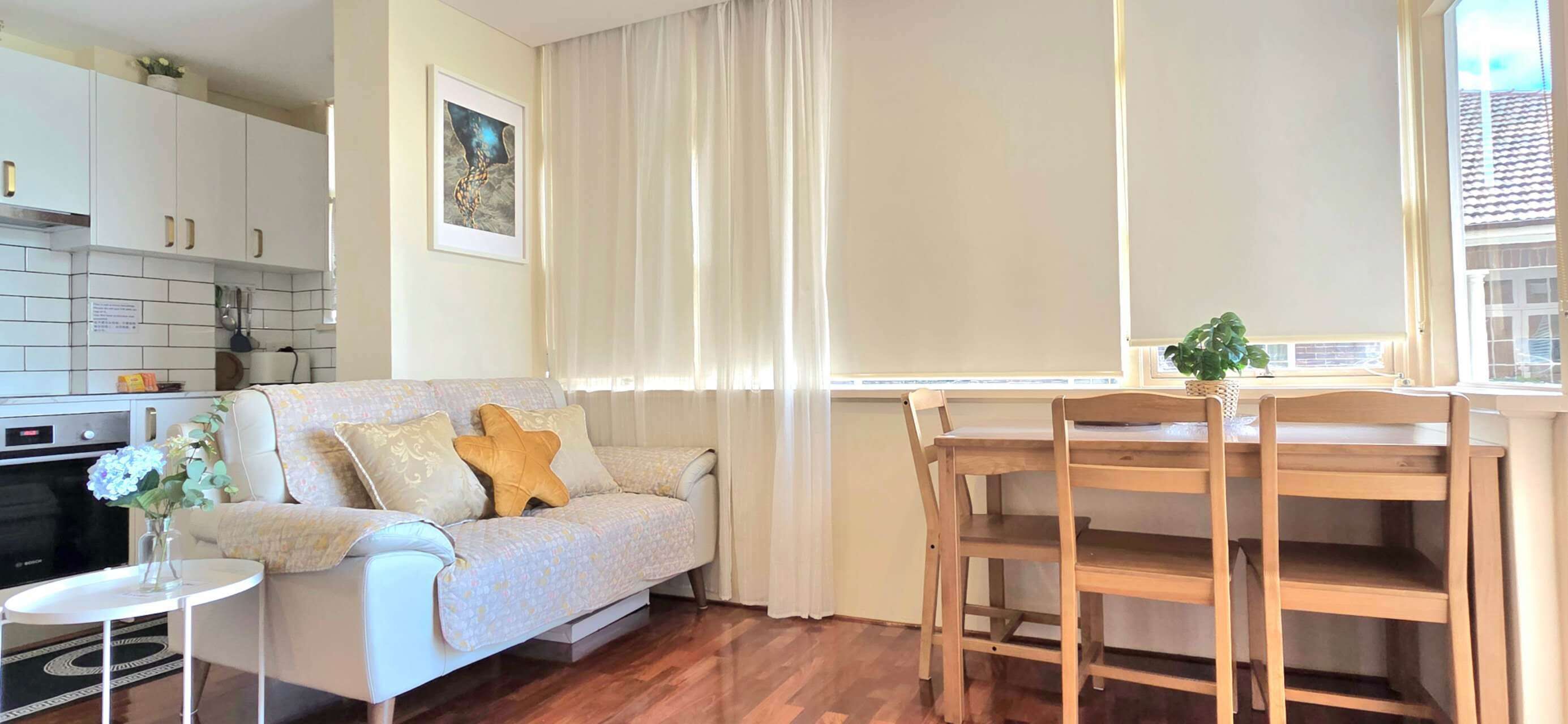 A compact living space with a kitchenette, a sofa with decorative pillows, a dining table with chairs, and a window with curtains.