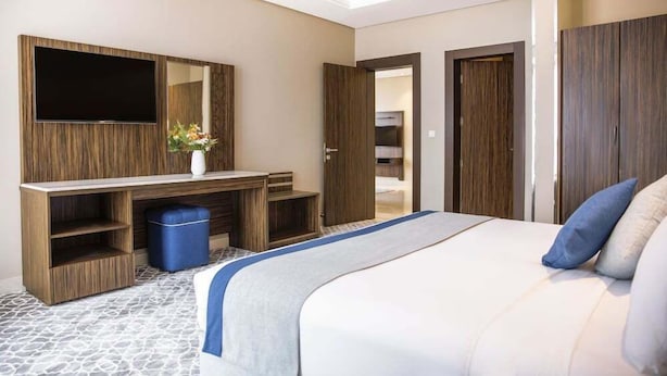 Una habitación de hotel con cama, televisor montado en la pared, escritorio con silla y armario.