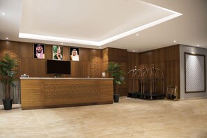 A hotel reception area with a wooden reception desk, a flat-screen TV, and a wall-mounted photo display. - Swiss Blue Heraa (Jeddah)