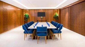 Un salón de conferencias con una mesa larga, sillas azules y un televisor de pantalla plana en la pared.