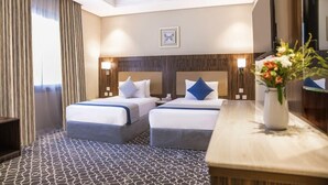 Habitación de hotel con dos camas, cabecera de madera, mesita de noche, un jarrón de flores y un espejo grande.