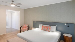 Quarto de hotel com cama, ventoinha no teto, uma cadeira e mesa de cabeceira.
