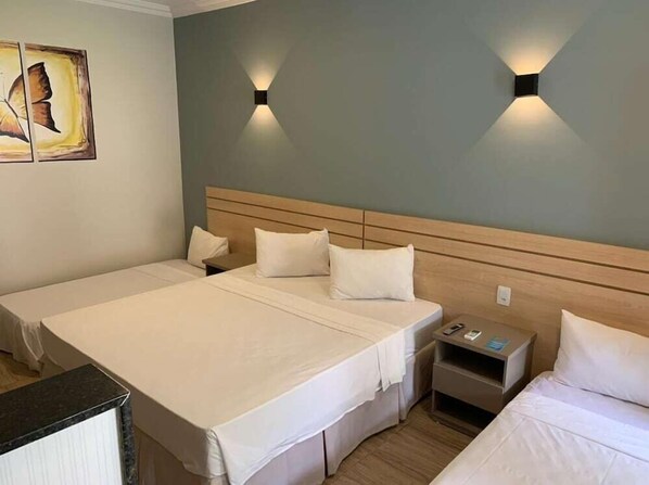 Habitación de hotel con dos camas, cabecero de madera, mesitas de noche e iluminación en la pared.