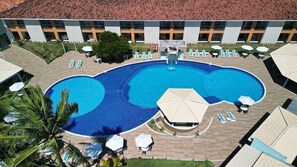 Una gran piscina al aire libre con varias zonas de descanso y sombrillas, rodeada por un edificio con tejado de cerámica.