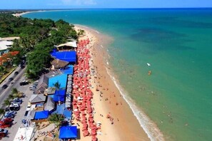 A beach with a row of blue-roofed structures and red umbrellas, likely a hotel or resort. - Porto Mar Hotel Porto Seguro (Porto Seguro)