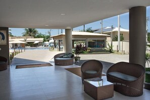 A covered outdoor area with wicker furniture, a pool, and a building with large windows. - Porto Mar Hotel Porto Seguro (Porto Seguro)