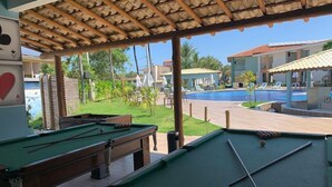 Ein Poolbereich mit mehreren Billardtischen, einem Schwimmbecken und einer überdachten Sitzgelegenheit mit Blick auf den Pool.