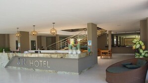 Eine Hotelhalle mit Empfangstresen, Sitzgelegenheiten, einer Treppe und einer großen Pflanze.