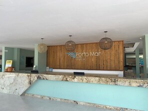 Zona de recepció d'un hotel amb un panell de paret de fusta, una taula de recepció i tres lluminàries esfèriques penjants.