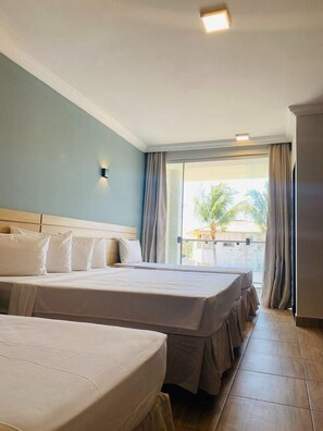 Habitació d'hotel amb dos llits, una finestra gran amb cortines i vista a palmeres a l'exterior.
