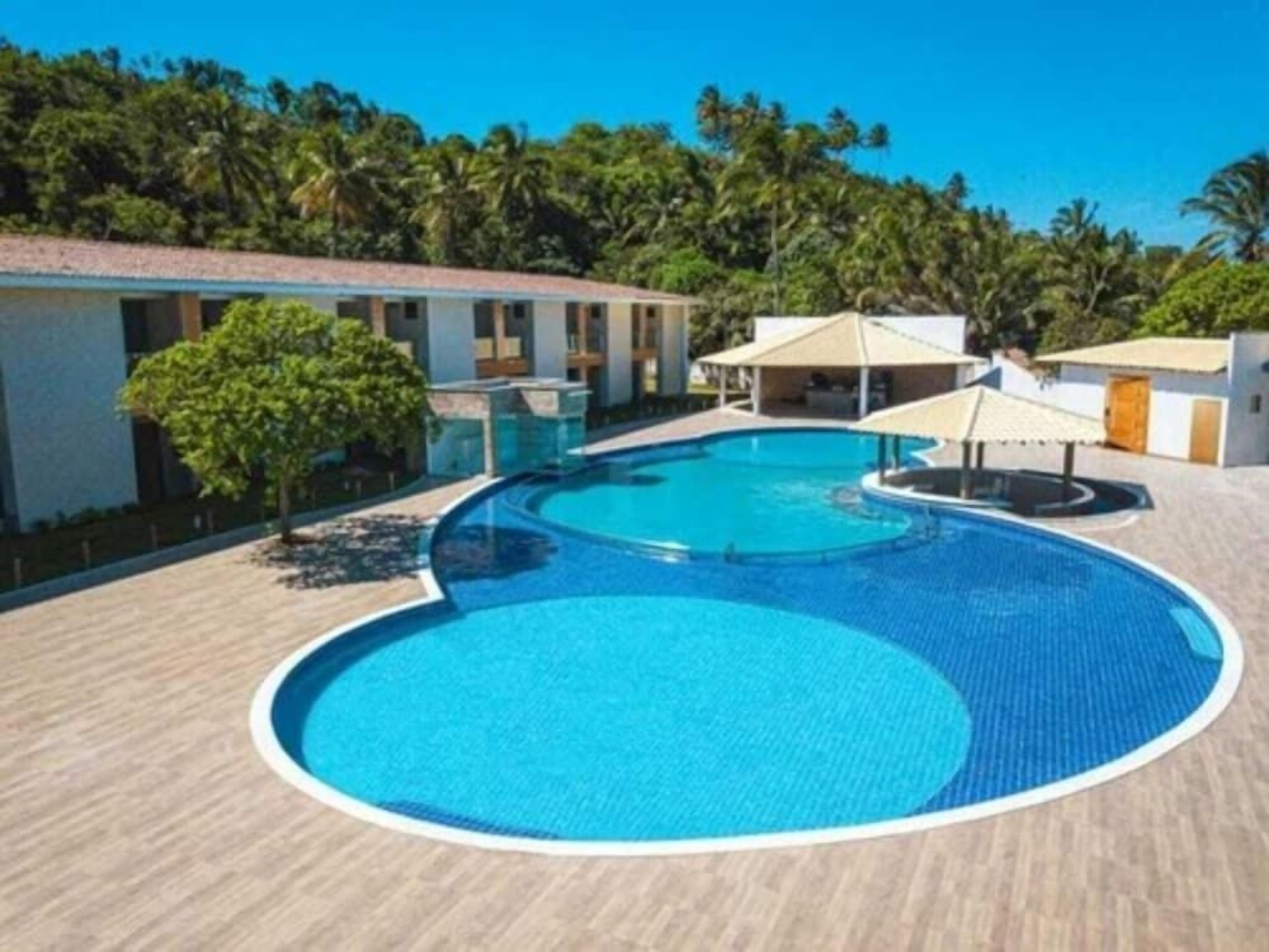 A swimming pool with a tiled deck, surrounded by buildings and palm trees.