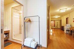 Ein Hotelzimmer mit Holzboden, einem Badezimmer mit Spiegel, einem Wäscheständer mit Handtüchern und einem Essbereich mit Tisch und Stühlen.