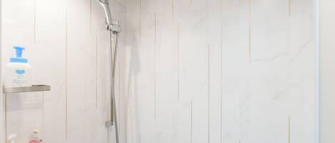 A bathroom with a shower, a soap dispenser, and a shampoo bottle on a shelf.