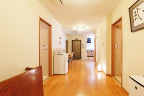 Un couloir d’hôtel avec un plancher en bois, un réfrigérateur, un four à micro-ondes et un coin repas comprenant des chaises et une table.